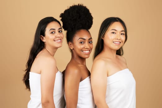 Three beautiful women of varied backgrounds pose confidently in white towels, showcasing their unique beauty and unity against soft beige background
