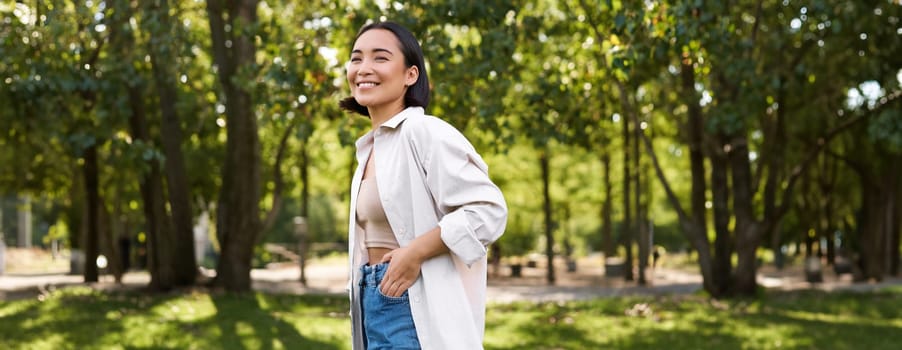 Modern people. Happy young asian girl walking in park, smiling and enjoying beautiful summer day.