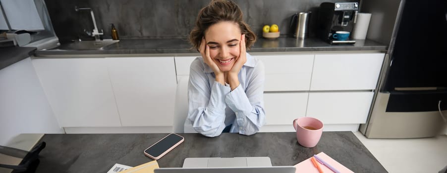 Beautiful self-employed girl works from home. Young woman online studying, watching course on website, looking at laptop screen.