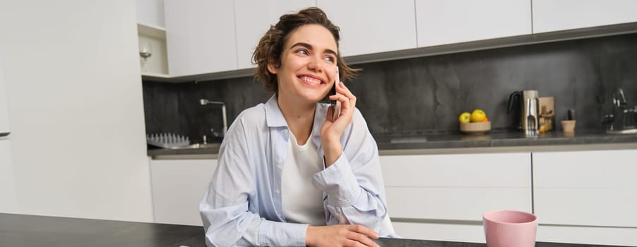 Portrait of cute smiling girl talks on mobile phone, sits at home and calls someone with smartphone.