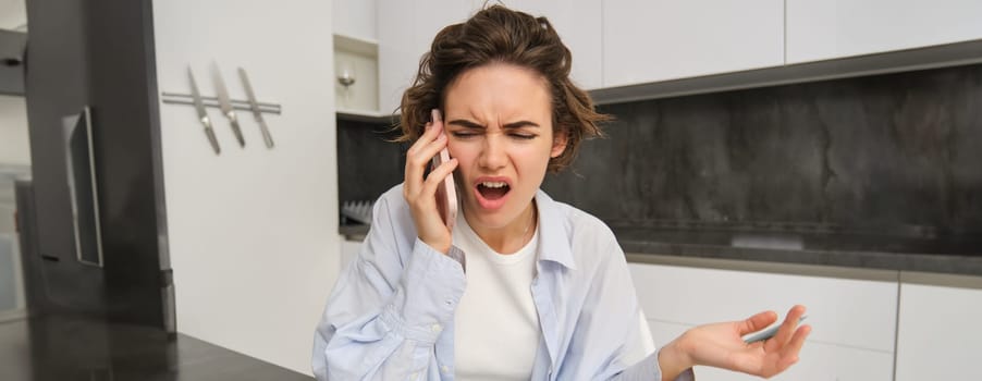 Portrait of woman arguing during phone call, complaining at someone over the telephone, sitting at home and shouting at smartphone.