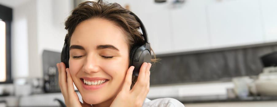 Close up portrait of cute young woman, smiling and listening to music in wireless headphones, enjoying good sound quality.