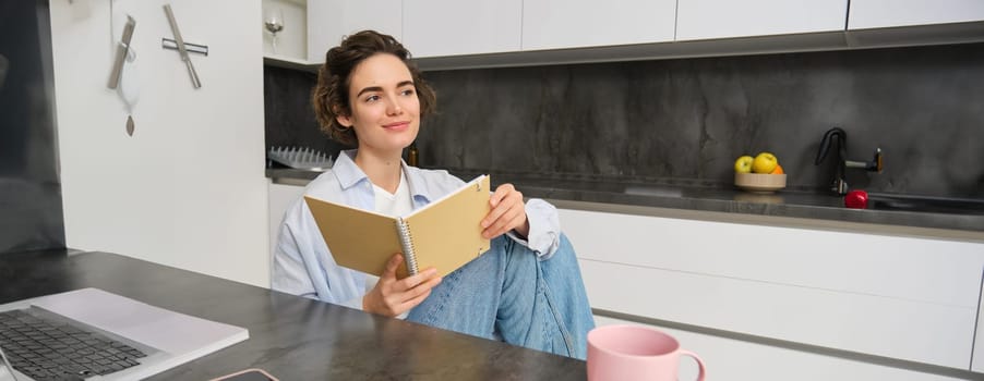 Lifestyle concept. Smiling brunette woman, sitting at home with notebook, reading notes, doing her homework at home.