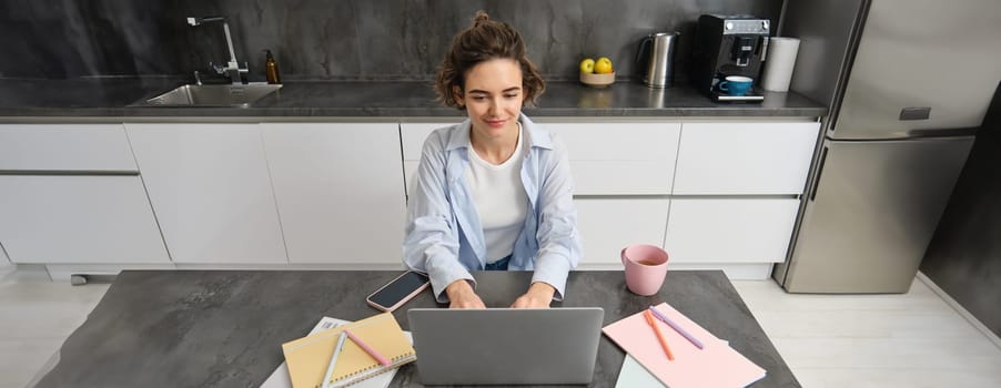 Beautiful self-employed girl works from home. Young woman online studying, watching course on website, looking at laptop screen.