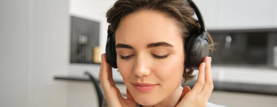 Close up portrait of woman face, listening to music in her wireless headphones with delight and pleasure, enjoying good sound quality in earphones.