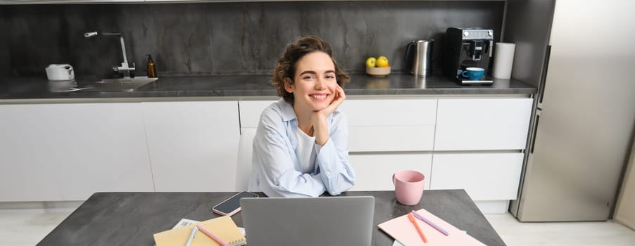 Beautiful girl with laptop, sitting at home and working on computer, doing her paperwork, studying online on remote. Copy space