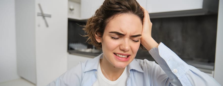 Portrait of brunette woman touches her head, grimaces from pain, has headache, painful migraine.