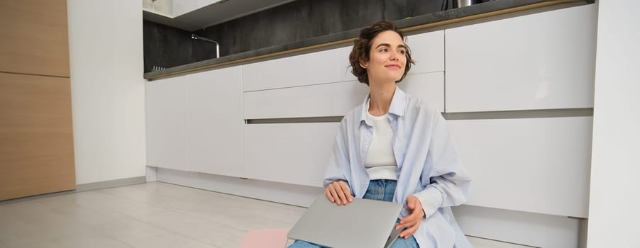 Young IT girl, woman works freelance from home, sits on floor with laptop. Girl student does homework online, writes on computer keyboard.