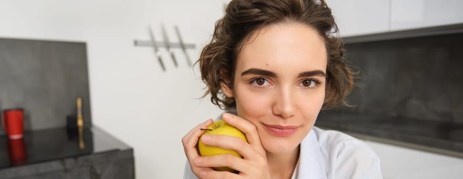 Close up portrait of healthy, beautiful young woman holding an apple, smiling. Lifestyle and people concept