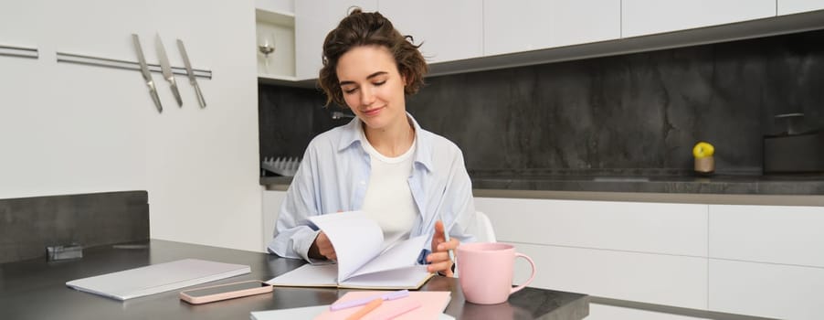 Portrait of young woman at home, working, writing in notebook, taking notes or doing homework.