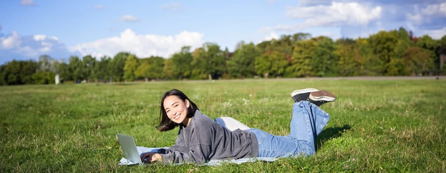 Leisure and people. Happy young woman lying in park on blanket, using laptop, relaxing outdoors and watching videos online on computer.