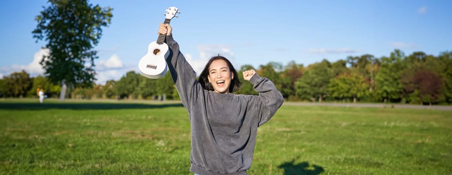 Positive beauty girl with ukulele, dancing and feeling freedom, looking excited, triumphing and celebrating.