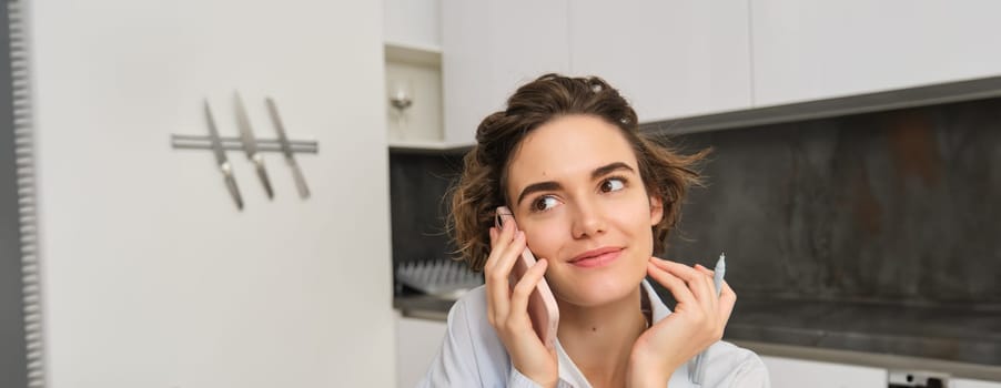 Portrait of beautiful girl talks on mobile phone, has conversation, answer a call in kitchen.