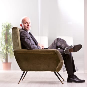 Mature businessman sitting on a very comfortable armchair relaxing and smiling at you