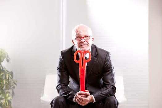 businessman thinking with a pair of red scissors in his hands