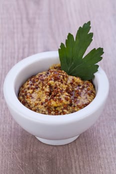 fresh yellow coarse-grained mustard with petersilie decorated in a white bowl detail