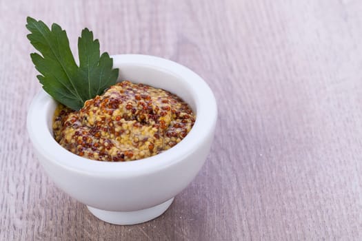 fresh yellow coarse-grained mustard with petersilie decorated in a white bowl detail