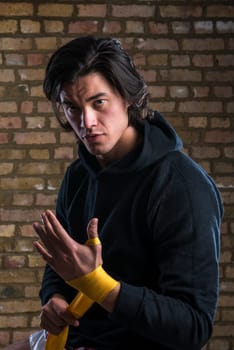 Young Malaysian boxer  wearing hoodie and wrapping straps around hands