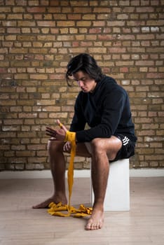 Young Malaysian boxer  wearing hoodie and wrapping straps around hands