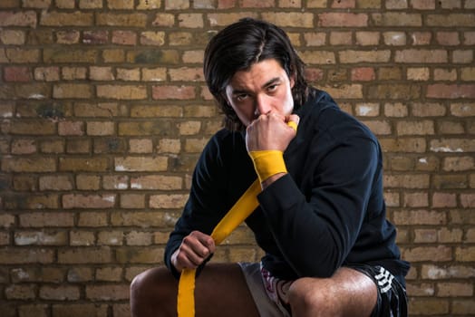 Young Malaysian boxer  wearing hoodie and wrapping straps around hands