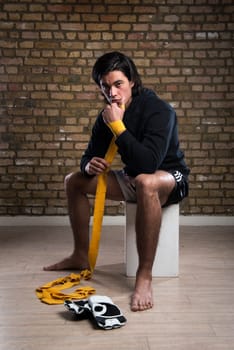 Young Malaysian boxer  wearing hoodie and wrapping straps around hands