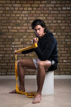 Young Malaysian boxer  wearing hoodie and wrapping straps around hands