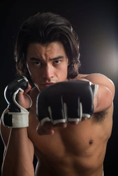 Bare chested young Malaysian boxer punching in the direction of the camera with fingerless gloves