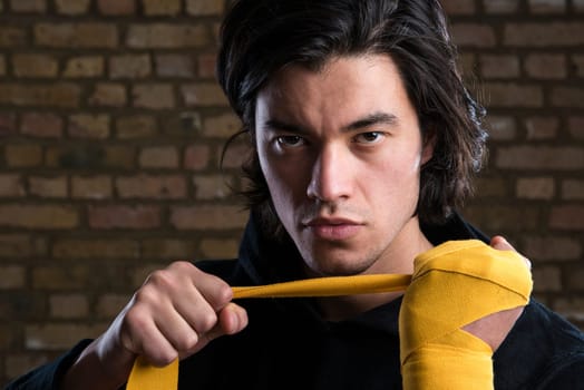Young Malaysian boxer  wearing hoodie and wrapping straps around hands