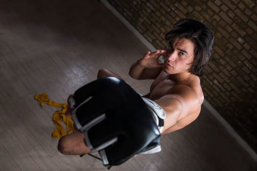 High angle shot of bare chested young Malaysian boxer punching in the direction of the camera with fingerless gloves
