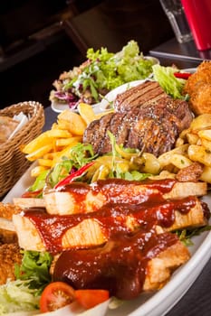 Huge barbecue plate with mixed meat and steaks on salad