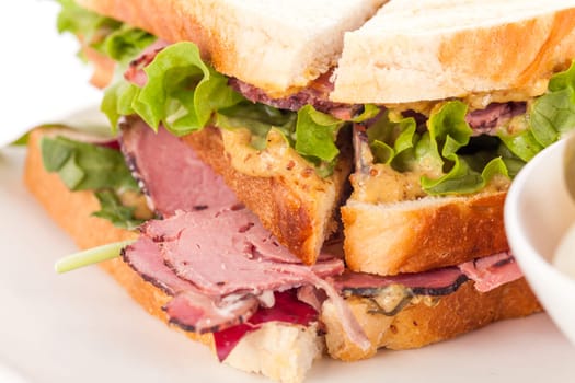 Delicious sandwich clubsandwich with bacon ham cheese and one with mixed pickels on a plate isolated against a white background