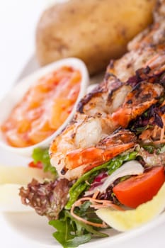 Roasted shrimp on a skewer on mixed salad with dip and foil potato prepared on a plate insulated against a white background