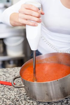 female chef in the restaurant kitchen gastronomy pureed passes tomatoes to a sauce puree tomato sauce
