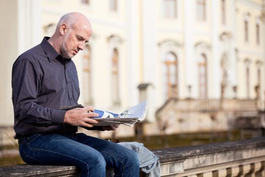 adult older man sitting outdoors reads a newspaper news free time