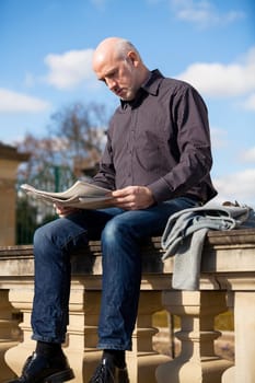 adult older man sitting outdoors reads a newspaper news free time