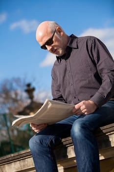 adult older man sitting outdoors reads a newspaper news free time