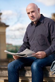 adult older man sitting outdoors reads a newspaper news free time