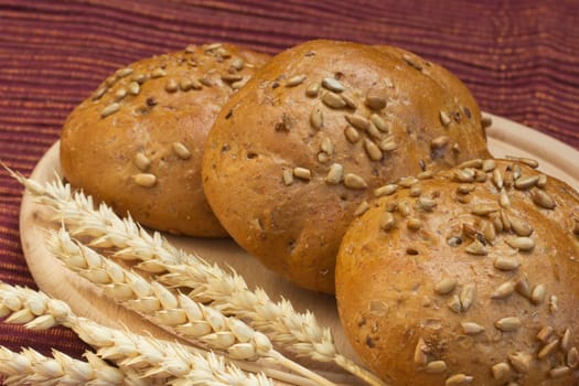 Wholemeal bread is  lying on a wooden tray on the table. Wheat ears are lying beside them.