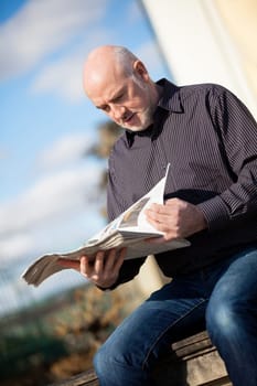 adult older man sitting outdoors reads a newspaper news free time