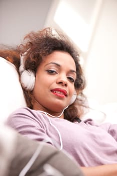 beautiful afroamerican woman on a sofa listenint to the music with her headphones