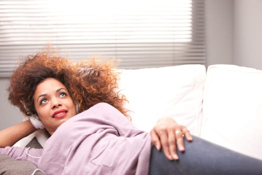 beautiful afroamerican woman on a sofa listenint to the music with her headphones