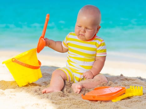 Cute baby on the tropical beach playing toys