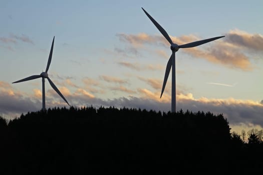 Silhouettes of two wind turbines behind a forest