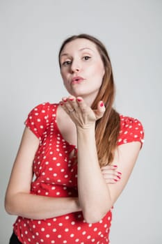 Studio portrait of attractive woman wearing spotty red blouse with pursed lips blowing a kiss