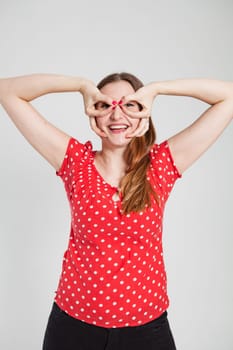 Studio portrait of smiling attractive woman wearing spotty red blouse looking through finger goggles