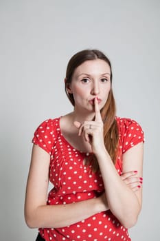 Studio portrait of attractive woman with finger over pursed lips to signal for quiet