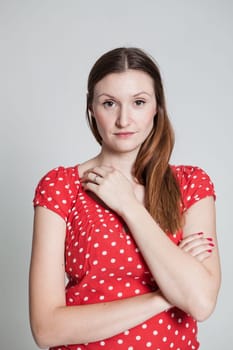 Studio portrait of relaxed and thoughtful looking attractive woman wearing spotty red blouse with arms folded