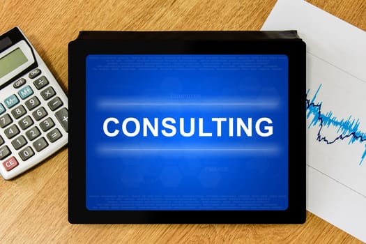 Consulting word on digital tablet with calculator and financial graph