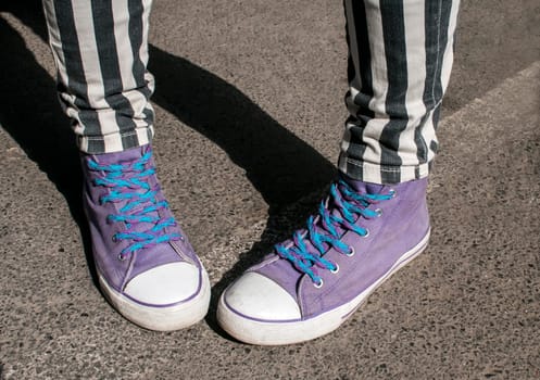 Girl legs with striped pants and purple sneakers on asphalt street surface