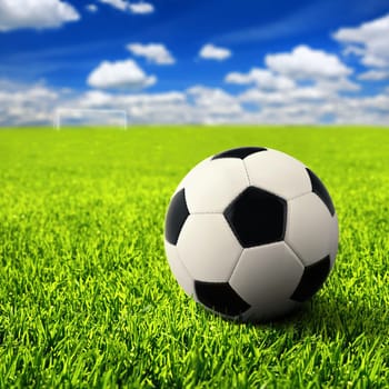 A football stands on a wide turf,in the distance the empty gate can be seen
